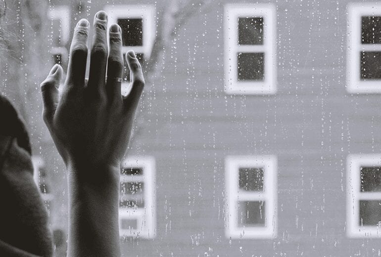 Woman's thin fraile hand pressed against a window with rain drops